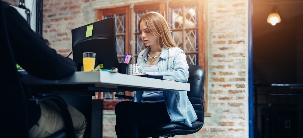 En kvinnlig marknadsförare sitter på kontoret, hon sitter vid skrivbordet, framför skärmen och använder sin dator.  