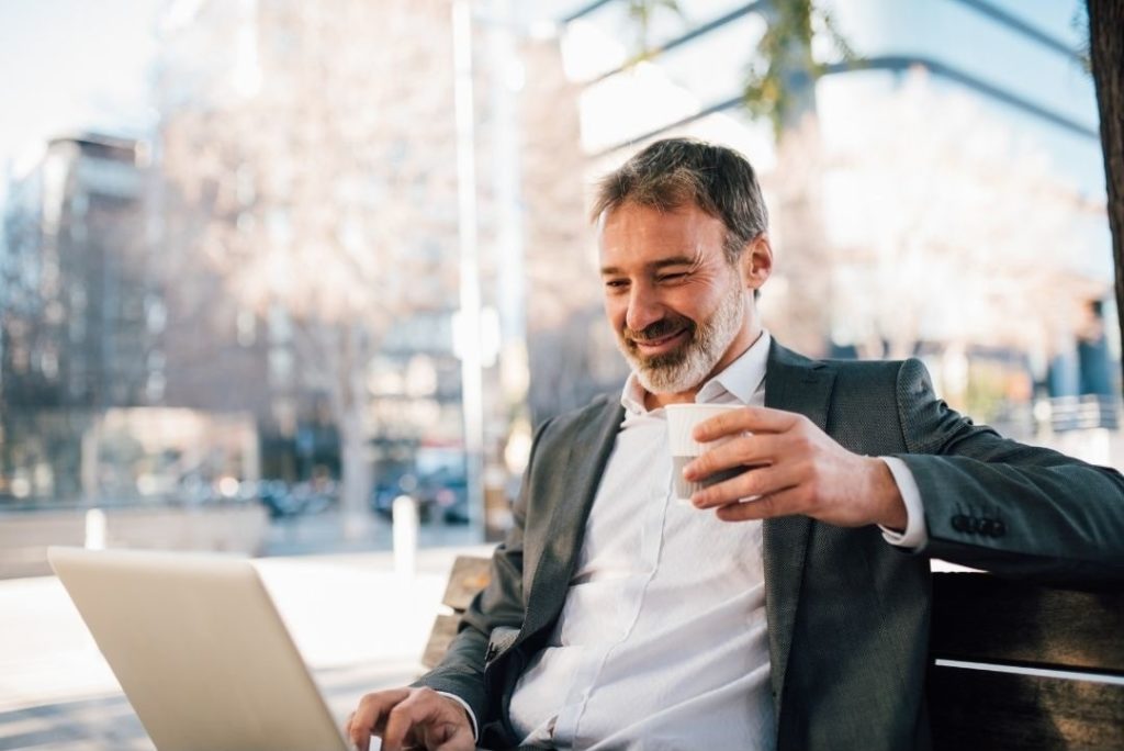 En medelålders man i kostym sitter vid datorn med en kopp kaffe.